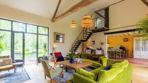 A spacious living area with a wooden floor, green sofas, a wooden coffee table, and a staircase leading to an upper level.