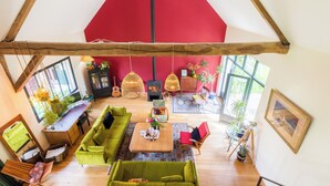 A spacious living area with a high ceiling, a red accent wall, and a wooden beam structure.