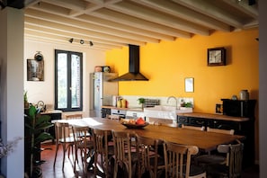 A kitchen with a wooden table, chairs, a black range hood, and a yellow wall.
