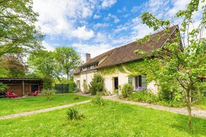 Una casa con jardín, zona de barbacoa y patio cubierto.