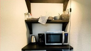 Una kitchenette compacta con microondas, cafetera y basurero.