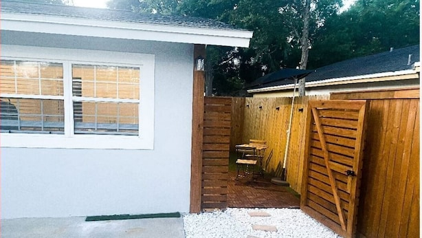 Una pequeña casa de exterior blanco, con un patio de concreto y cerca de madera.