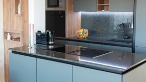 A modern kitchen with a granite countertop, stainless steel appliances, and a built-in microwave. - Penthouse Rosa (Radici)