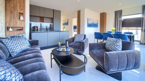 A modern living room with grey sofas, a black coffee table, and a kitchen area in the background. - Penthouse Rosa (Radici)