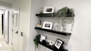 A hallway with a white door, a black shelf with framed photos and a small plant, and a wall-mounted picture frame. - Cozy fully renovated townhome,free parking. Minutes away from Whistler Village. (Whistler)