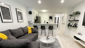 A modern living room with a grey sectional sofa, two black bar stools, a marble coffee table, and a kitchen in the background. - Cozy fully renovated townhome,free parking. Minutes away from Whistler Village. (Whistler)