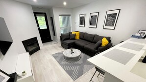 A modern living room with a grey sofa, a coffee table, and a fireplace. There are framed pictures on the wall and a window with blinds. - Cozy fully renovated townhome,free parking. Minutes away from Whistler Village. (Whistler)
