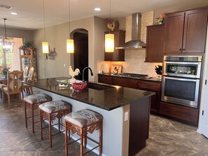 A kitchen with a large island, bar stools, a double oven, and a backsplash with a brick pattern.