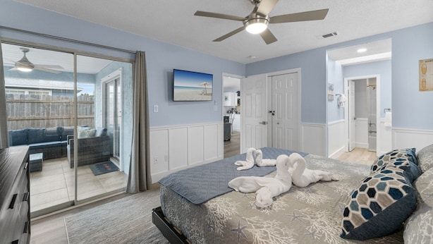 A bedroom with a bed, a ceiling fan, a sliding glass door leading to a balcony, and a view of the beach. - Fall Special! 3BR - Walk to Beach, Private Yard, Fire Pit, Dog Friendly! (Panama City Beach)