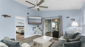A living room with a ceiling fan, a sofa, a coffee table, and a TV. - Fall Special! 3BR - Walk to Beach, Private Yard, Fire Pit, Dog Friendly! (Panama City Beach)