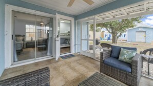 A covered patio area with a ceiling fan, sliding glass doors leading to a bedroom, and outdoor furniture. - Fall Special! 3BR - Walk to Beach, Private Yard, Fire Pit, Dog Friendly! (Panama City Beach)