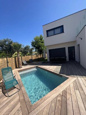 Una casa moderna de dos pisos con una terraza de madera y una piscina.