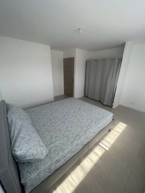Un dormitorio minimalista con una cama individual, una puerta y una cortina.
