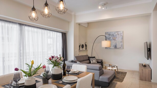 Un salon moderne comprenant un coin repas, un canapé gris, une table basse et un téléviseur fixé au mur.