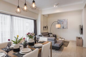 Una sala de estar moderna con comedor, un sofá gris, una mesa de centro y un televisor montado en la pared.