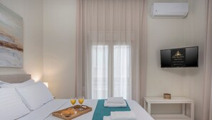 Une chambre d’hôtel avec un lit, un plateau avec des croissants et du jus d’orange, un téléviseur fixé au mur et une fenêtre avec des rideaux légers.