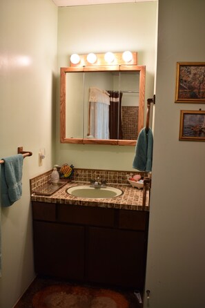 Une salle de bain avec un lavabo, un miroir et un meuble-lavabo. Deux serviettes sont accrochées au mur et on aperçoit un rideau de douche dans le reflet du miroir.