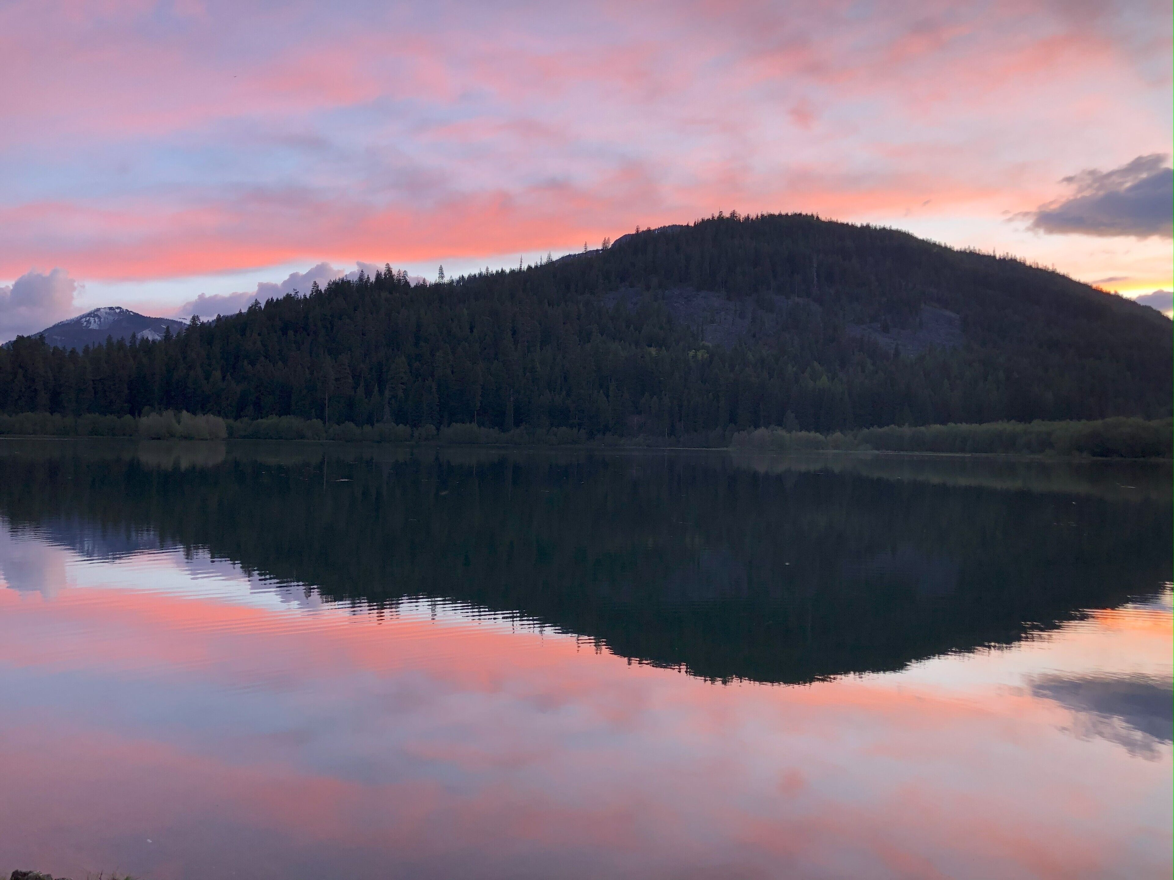 A calm lake reflecting a forested mountain at sunset.