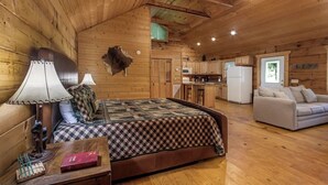 Interior de una cabaña de troncos con una cama, un sofá, una zona de comedor y una cocina.