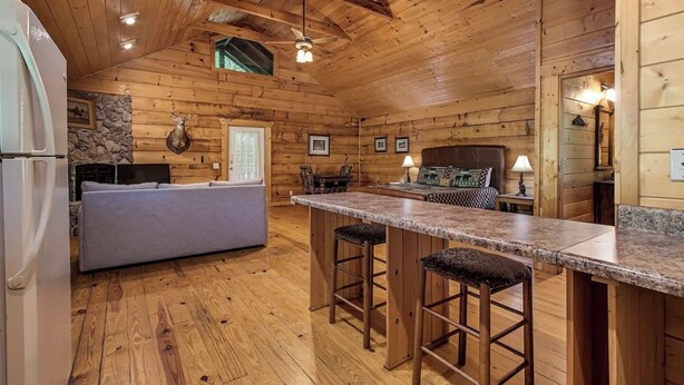 Interior de una cabaña de troncos con cocina, que incluye una chimenea de piedra, una mesa de comedor y una barra con taburetes.