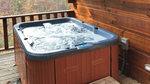 Un jacuzzi en una terraza de madera, con un muro de cabaña de madera al fondo.