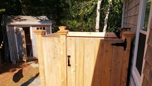 A wooden fence with a metal latch, a gravel path, and a shed in the background.