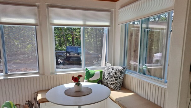 A sunroom with a white table, a bench with cushions, and a view of the outside.