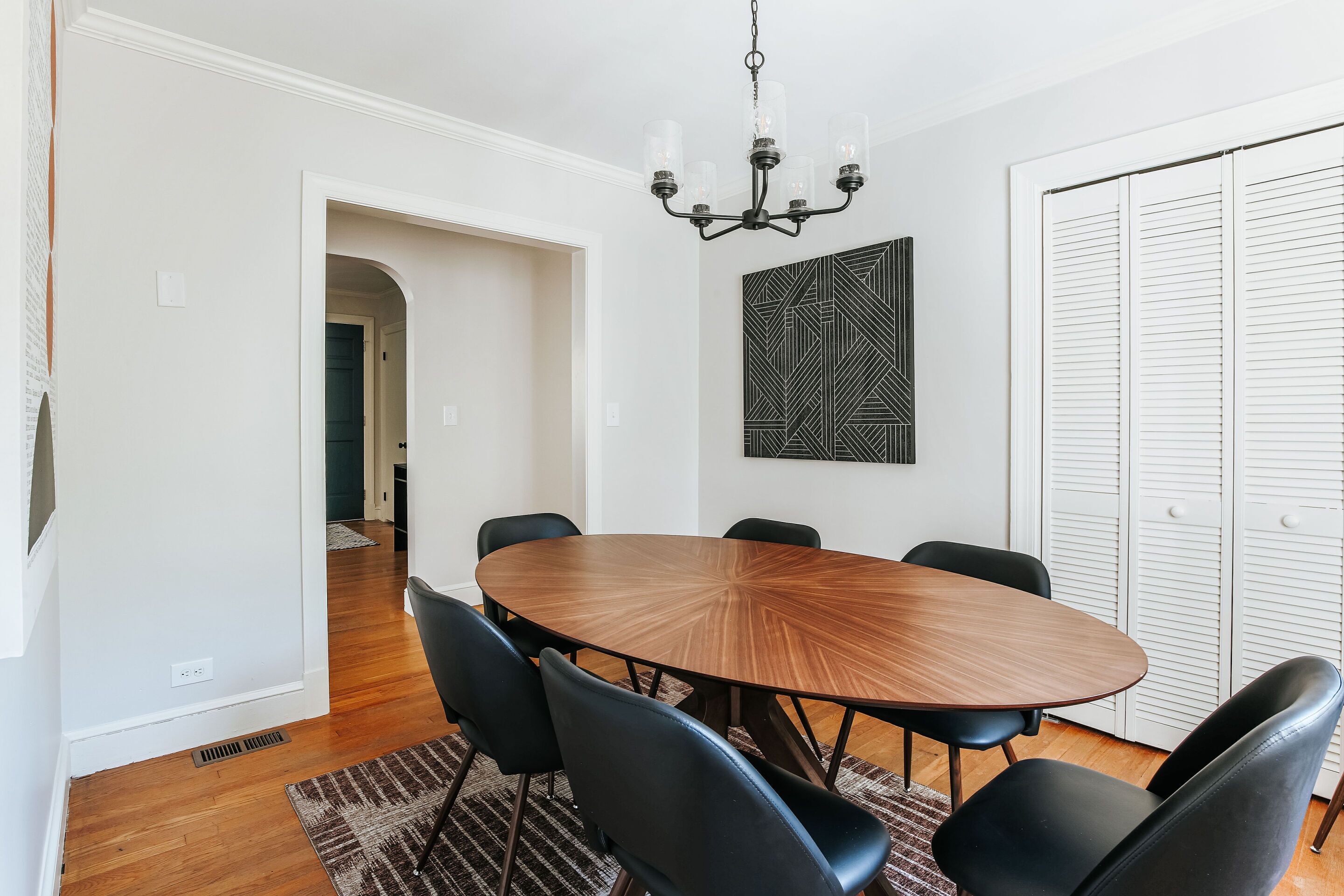 A dining area with a round table, black chairs, a chandelier, and a geometric wall art piece.