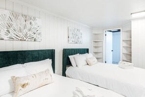 A hotel room with two beds, white bedding, and a green headboard. There are decorative wall art pieces and a visible closet with shelves. - Lewis Mtn Midterm: 31+ days, Walk to UVA (Charlottesville)