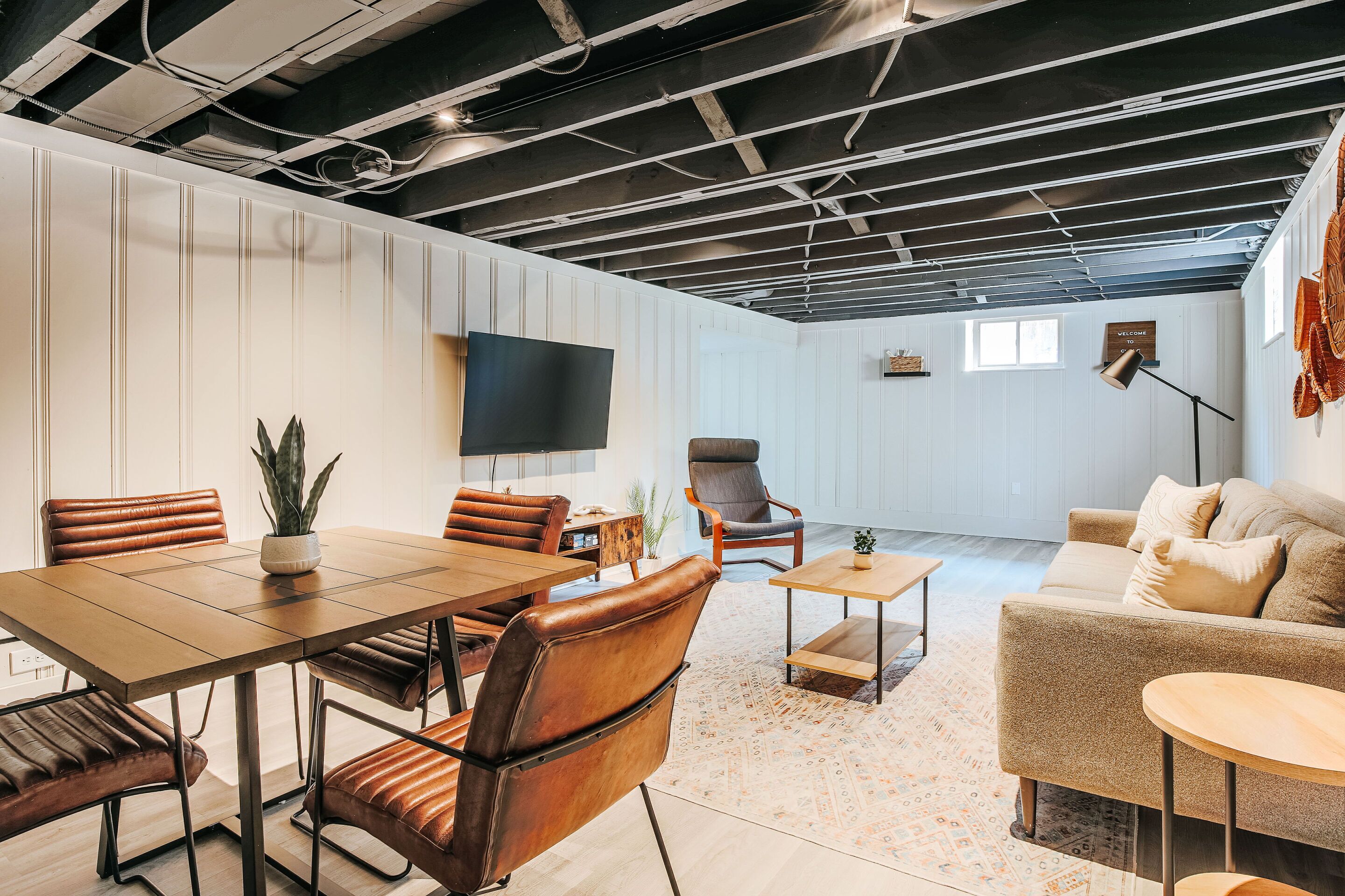 A modern interior with a dining area, a sofa, a TV, and a ceiling with exposed beams.