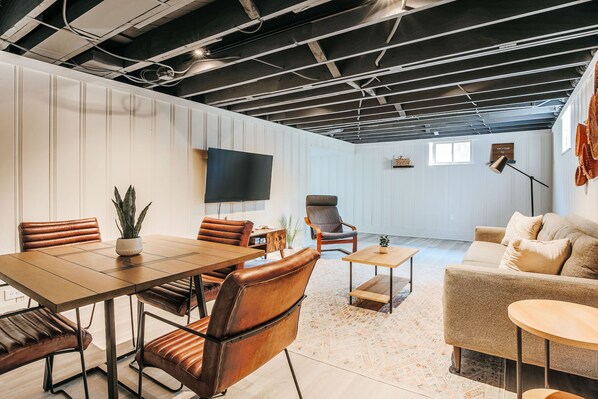 Ein modernes Interieur mit Essbereich, einer Couch, einem Fernseher und einer Decke mit freiliegenden Balken.
