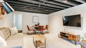 En moderne stue med spiseplads, et fladskærms-tv og et loft med synlige bjælker.