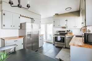 A modern kitchen with stainless steel appliances, white cabinetry, and a wooden countertop.