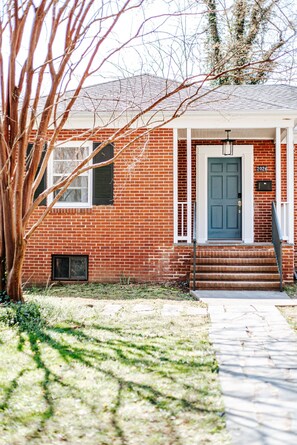 A red brick house with a blue door, white porch, and steps leading to the entrance.