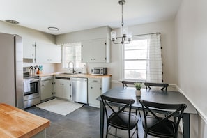 Una cocina con armarios blancos, microondas, fregadero y comedor con mesa y sillas.