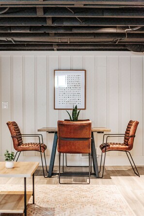 A room with a wooden table, two leather chairs, a potted plant, and a framed artwork on the wall.
