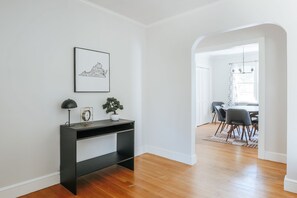 A modern room with a wooden floor, a black desk with a lamp, a framed picture, and a potted plant.