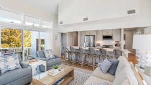 A spacious living area with a large sofa, a coffee table, and a dining area with chairs and a kitchen in the background. - Newly Remodeled, 5 BR, across from South Beach.  Shoals & BHI Clubs available (Bald Head Island)