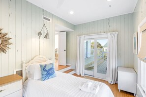 A bedroom with a bed, bedside table, and a view of the outside through a sliding glass door. - Newly Remodeled, 5 BR, across from South Beach.  Shoals & BHI Clubs available (Bald Head Island)