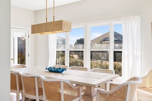 A dining area with a white table and wicker chairs, large windows with white curtains, and a hanging light fixture. - Newly Remodeled, 5 BR, across from South Beach.  Shoals & BHI Clubs available (Bald Head Island)