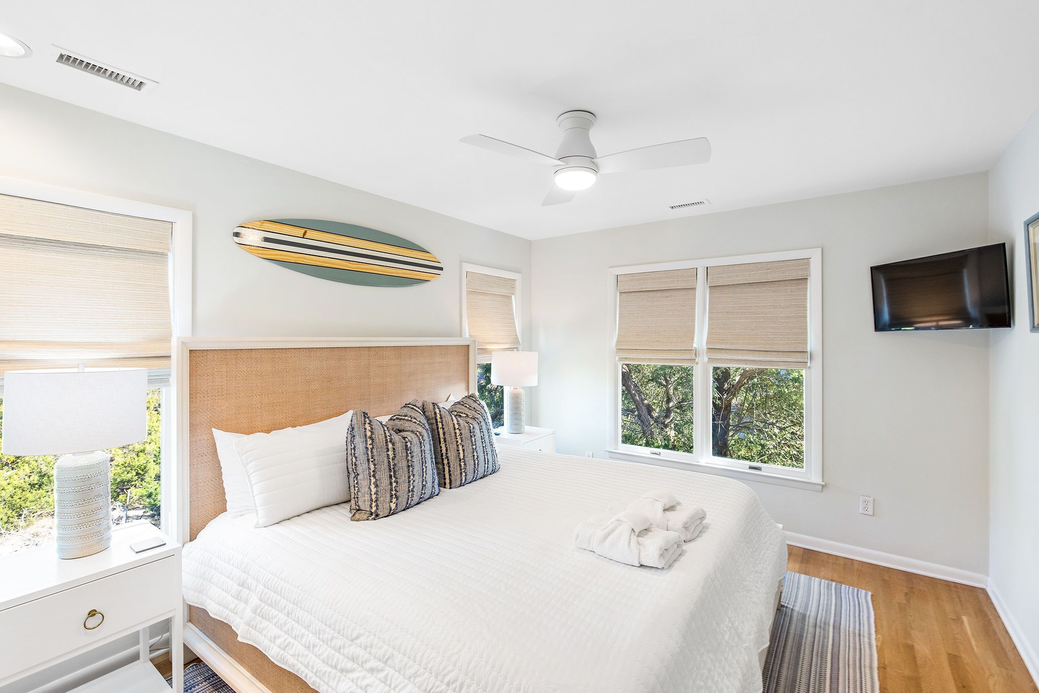 Un dormitorio con cama, ventilador de techo, televisor y ventanas con persianas.