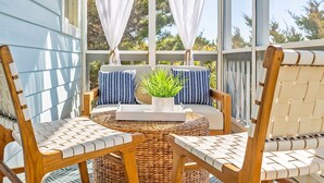 A covered outdoor seating area with wicker chairs and a woven table, featuring a potted plant and striped cushions. - Newly Remodeled, 5 BR, across from South Beach.  Shoals & BHI Clubs available (Bald Head Island)