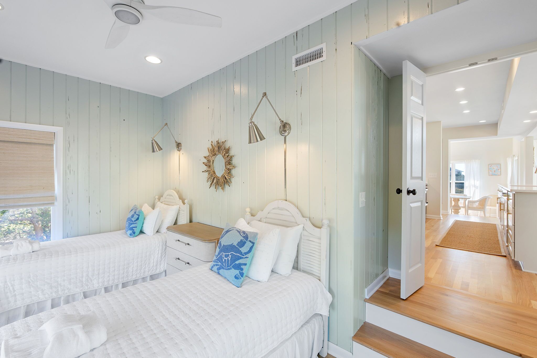 A bedroom with two beds, a ceiling fan, and a view of the adjacent kitchen.