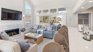 A spacious living room with a fireplace, comfortable seating, a dining area, and large windows offering a view of the outdoors. - Newly Remodeled, 5 BR, across from South Beach.  Shoals & BHI Clubs available (Bald Head Island)