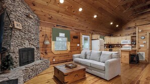 Interior acolhedor de uma cabana com lareira de pedra, um sofá branco e uma mesa de jantar de madeira.