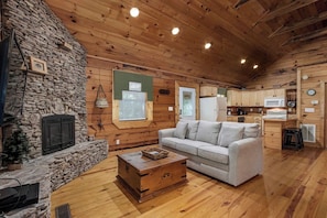 Interior acogedor de una cabaña con chimenea de piedra, un sofá blanco y una mesa de comedor de madera.