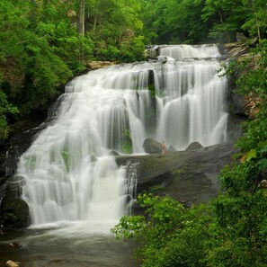 A waterfall cascading over a rocky terrain surrounded by dense green foliage. - Angler cabin. This modern private studio Cabin with HOT TUB is tucked away in a wooded cove. (Tellico Plains)