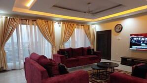 A living room with red sofas, a coffee table, and a TV displaying a news channel. - 2,3 Ensuite Bedrooms Luxury Staycation and Vacation apartments (Kasoa)