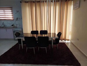 A dining area with a table and four chairs, a washing machine, and a window with blinds. - 2,3 Ensuite Bedrooms Luxury Staycation and Vacation apartments (Kasoa)