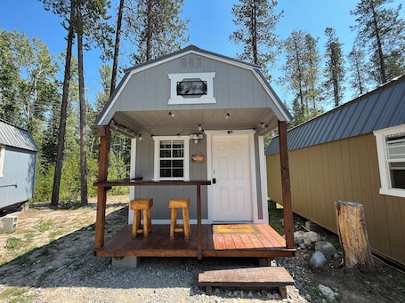 A small cabin with a porch, two wooden stools, and a welcome mat.
